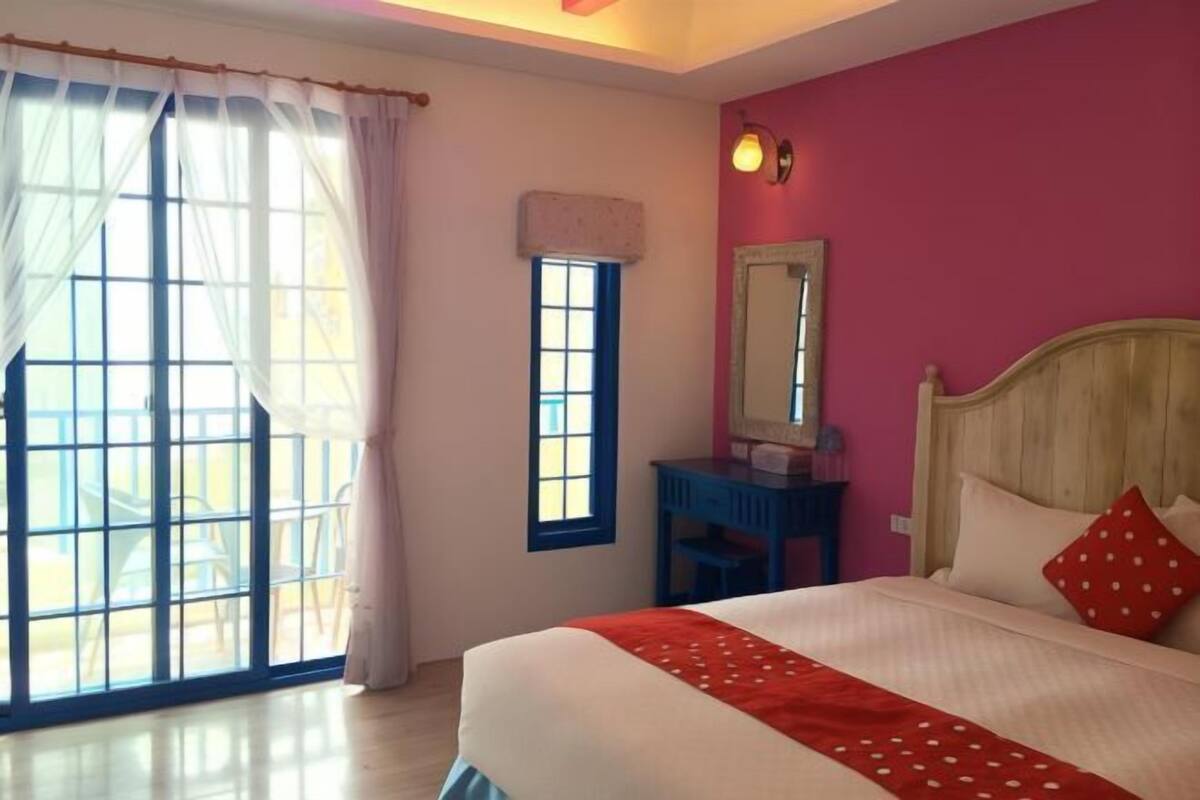 A bedroom with a bed, a window, a desk, and a mirror.