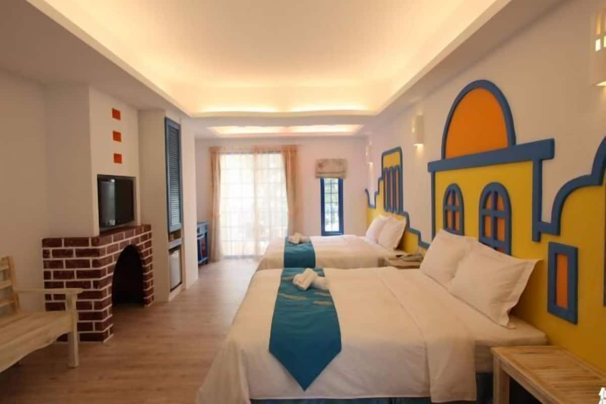 A hotel room with two beds, a TV, a fireplace, and a window with curtains.