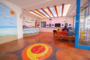 A reception area with a counter, seating, and a mural of a beach scene. - Meet Kenting Hostel (Pingtung)