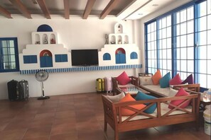 A living room with a sofa, colorful cushions, a television, and a fan. - Meet Kenting Hostel (Pingtung)