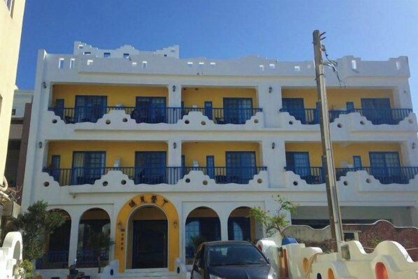 A multi-story building with balconies, a central entrance, and a parked car.