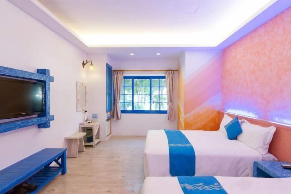 A hotel room with two beds, a TV, a desk, and a window with curtains.