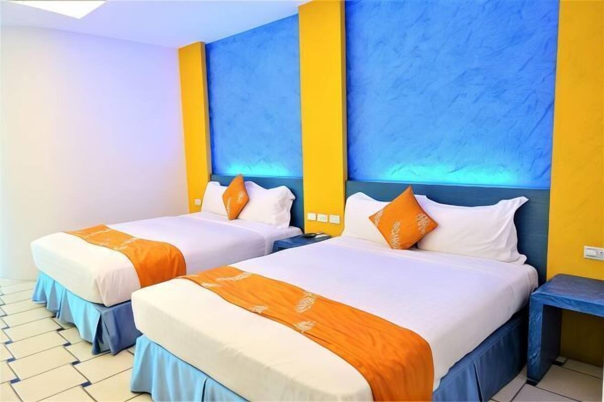 A hotel room with two beds, each with an orange and white bedspread, and a blue accent wall.