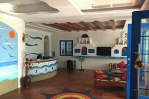 A reception area with a desk, a blue door, and a wall with a mural. - Meet Kenting Hostel (Pingtung)