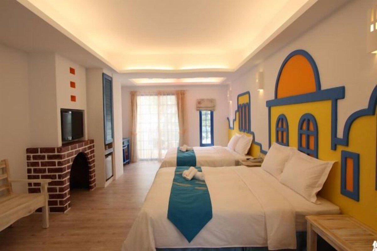 Una camera d'albergo con due letti, televisione, camino e una grande finestra con tende.