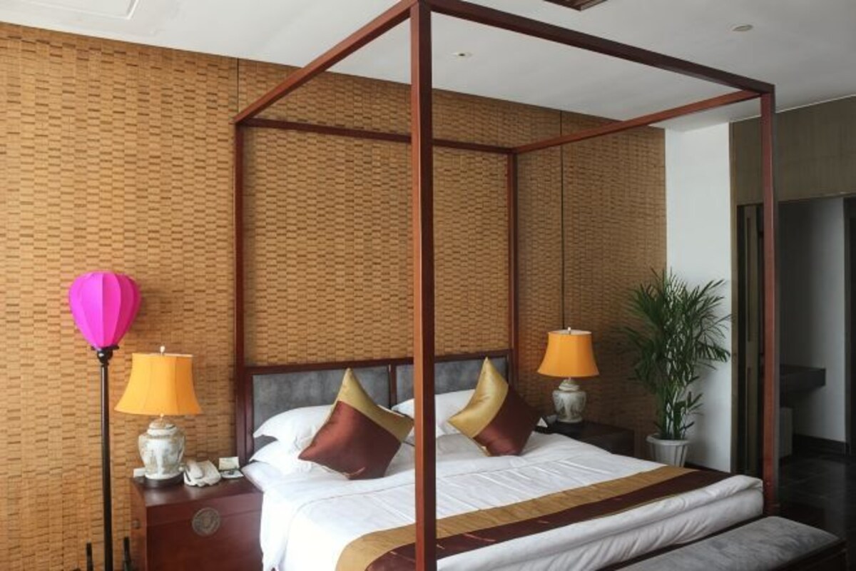 Una cama con dosel, dos lámparas de noche, un teléfono y una planta en maceta.