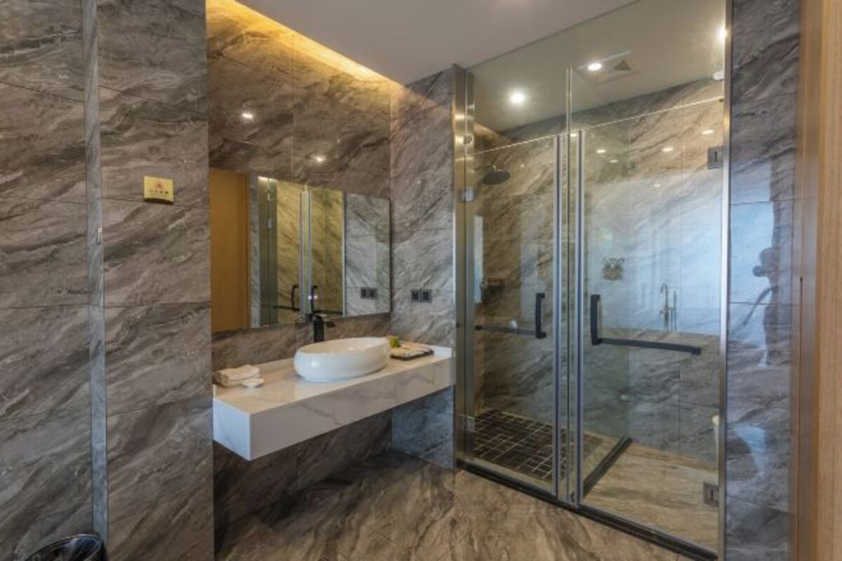 Un baño moderno con pared de mármol, lavamanos blanco y ducha con cerramiento de vidrio.