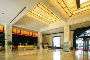 Un hall d’entrée spacieux avec un plafond haut, un comptoir de réception et plusieurs plantes en pot.