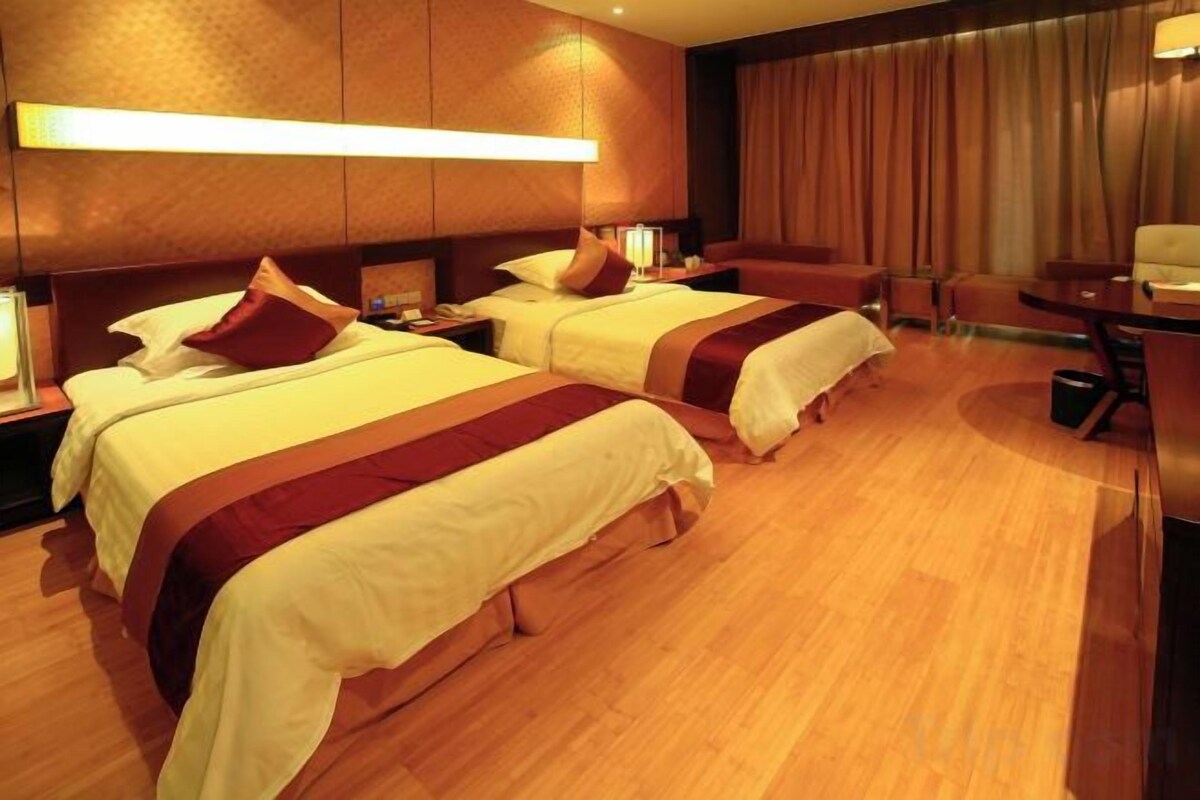 A hotel room with two beds, wooden flooring, and a large window with curtains.