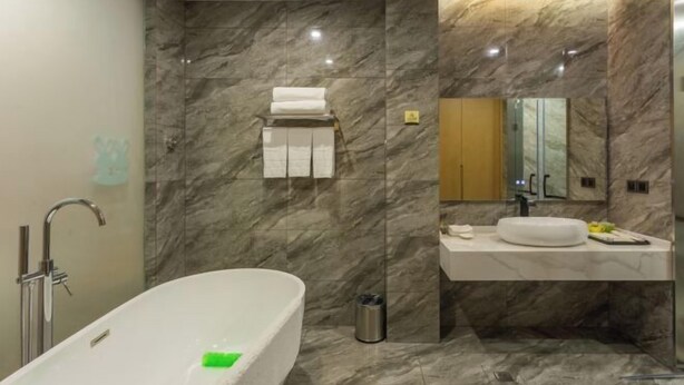 A modern bathroom with a freestanding bathtub, a vanity with a mirror, and marble walls.