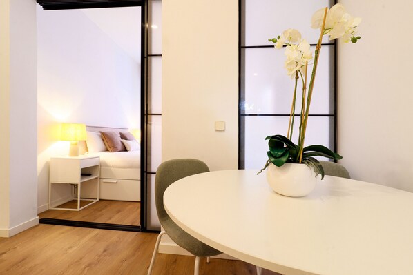 A modern room with a round dining table, a green chair, a white sofa, and a white lamp. - ChicLavapies Center (Madrid)