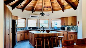Une cuisine spacieuse avec un haut plafond en bois, de grandes fenêtres et un îlot central doté de tabourets.