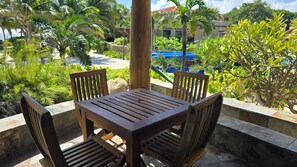 A wooden table and chairs on a balcony with a view of a pool and greenery. - Seascape Villas Belize (San Pedro)
