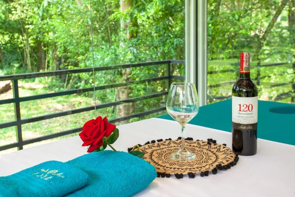 A table with a bottle of wine, a glass, a red rose, and a blue towel.