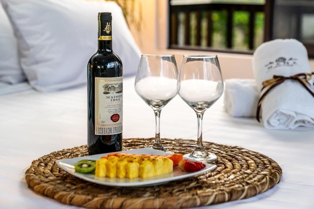 A bottle of wine, two glasses, and a plate with fruit on a bed.