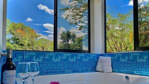 A bathroom with a bathtub, a bottle of wine, two glasses, and a plate with a slice of cake and flowers. - Hotel Nana  (Villeta)