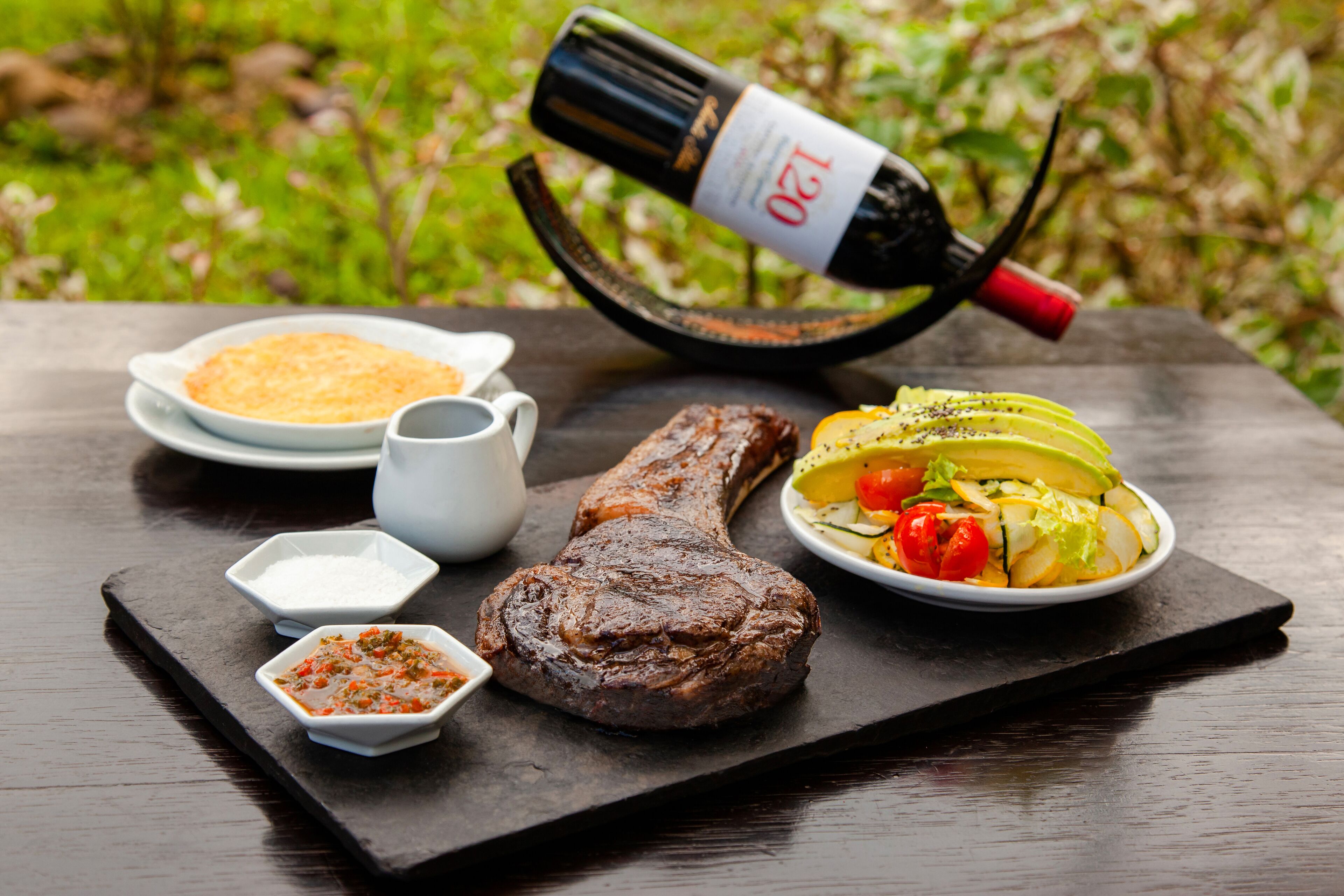 A meal with steak, vegetables, and a bottle of wine on a slate board.