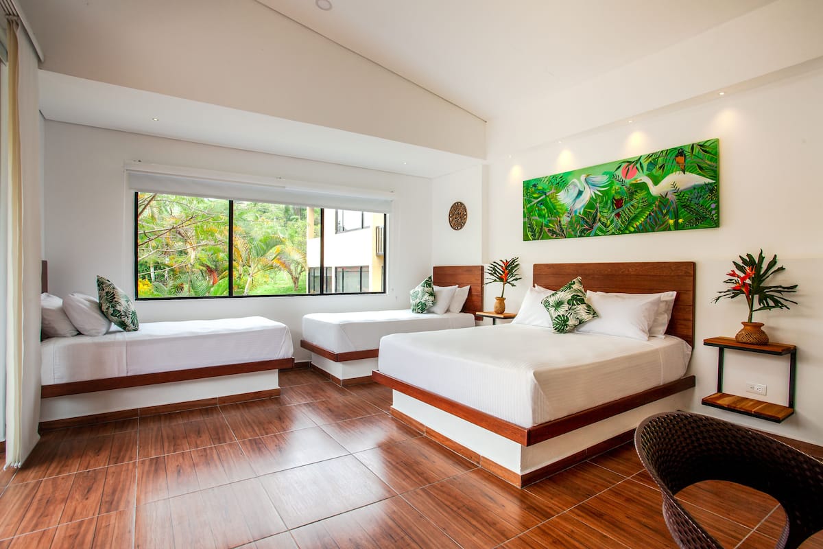 A modern hotel room with a large window, a bed, a sofa, and a chair.