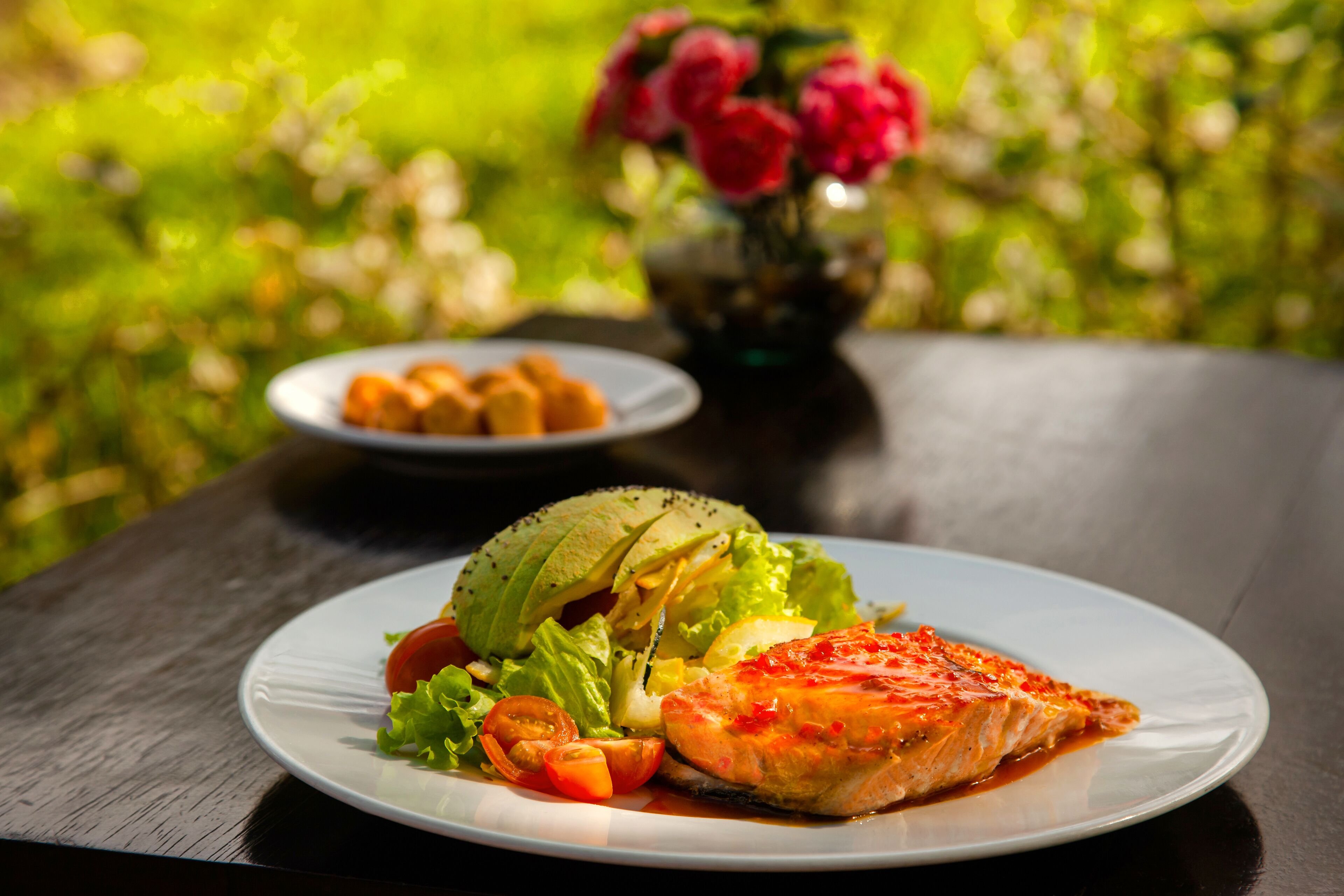 Un plato de comida con una porción de salmón, aguacate, lechuga y tomates cherry sobre una mesa de madera.