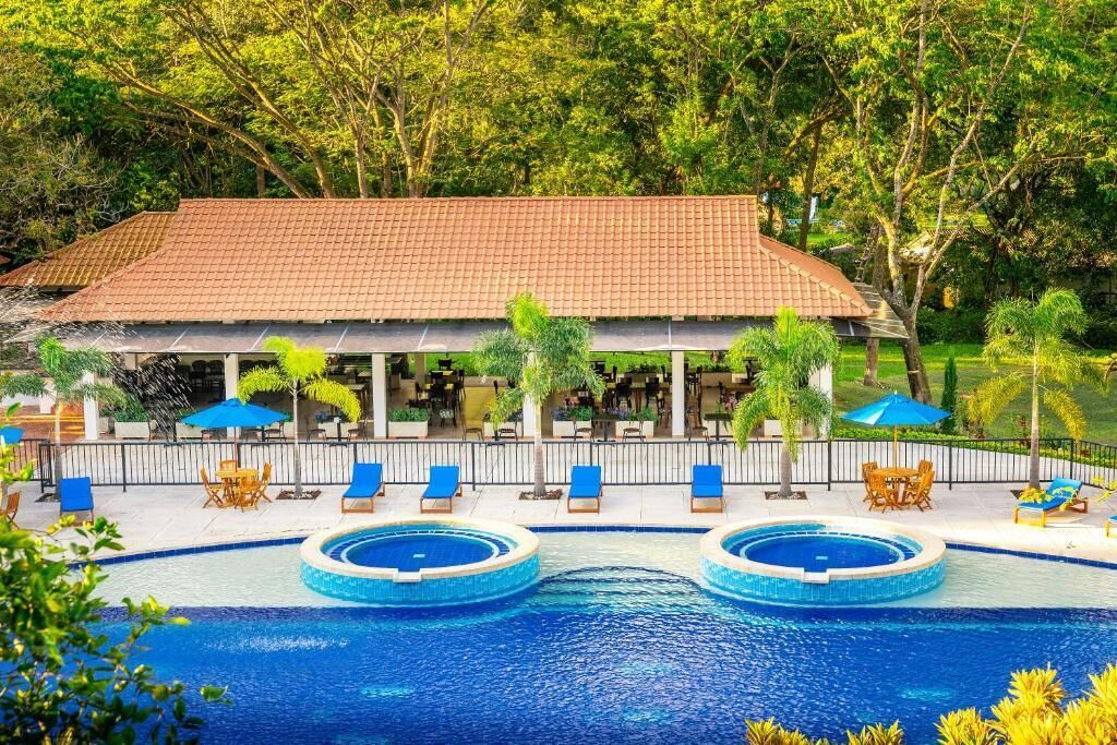A resort with a swimming pool, lounge chairs, and a covered area with tables and umbrellas.
