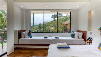 A hotel room with a large window, a bed, a seating area with pillows, and a phone on the nightstand.