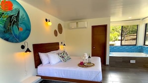 A bedroom with a bed, bedside lamps, a wall art piece, a small table with a tray, and a window with a view of the outdoors. - Hotel Nana  (Villeta)