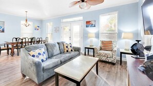 Ein Wohnzimmer mit grauem Sofa, einem Couchtisch, einem gemusterten Sessel und einem Deckenventilator.