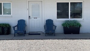 Una casa con una porta bianca con la scritta 'PRIVATE', due poltrone Adirondack blu e due piante in vaso sul portico.