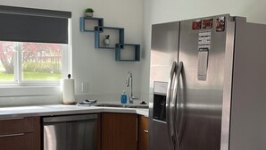 Una cucina moderna con frigorifero in acciaio inossidabile, mobili in legno, un piano di lavoro bianco e una finestra vista verde.