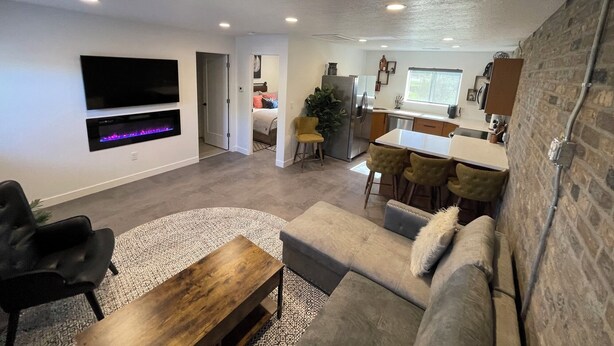 A modern living room with a flat-screen TV, a fireplace, a sofa, and a dining area with a kitchen in the background. - Modern, One Bedroom Apartment in Bryce Canyon Country, Panguitch, Utah (Panguitch)