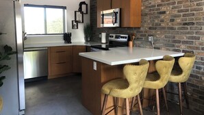 A modern kitchen with wooden cabinets, a stainless steel refrigerator, a built-in oven, and a bar area with two stools. - Modern, One Bedroom Apartment in Bryce Canyon Country, Panguitch, Utah (Panguitch)