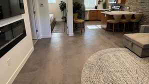 A modern kitchen with a brick accent wall, a dining area with yellow chairs, and a living room with a large TV and a patterned rug. - Modern, One Bedroom Apartment in Bryce Canyon Country, Panguitch, Utah (Panguitch)