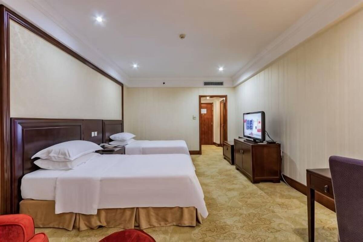 Ein Hotelzimmer mit zwei Betten, einem Fernseher, einem Schreibtisch und einem Sessel.