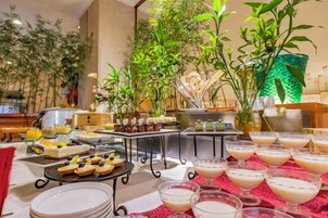 Montaje de bufé con diferentes alimentos y bebidas, rodeado de plantas de interior y una estructura decorativa verde.