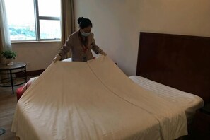 Een bed met een beigekleurige matras, een houten hoofdbord en een raam met uitzicht.