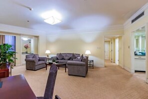 A spacious living area with a sofa set, a coffee table, and a dining table. There is a potted plant and a lamp on the side table.
