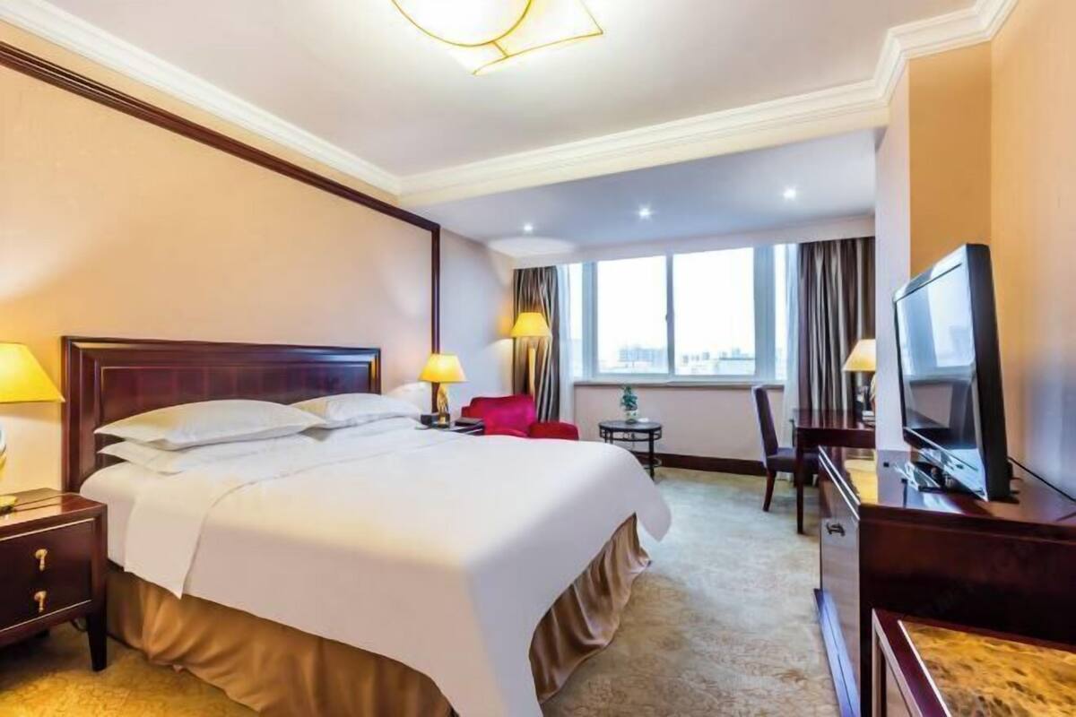 Ein Hotelzimmer mit einem großen Bett, Nachttischen, einem Fernseher, einem Schreibtisch und einem Fenster mit Vorhängen.