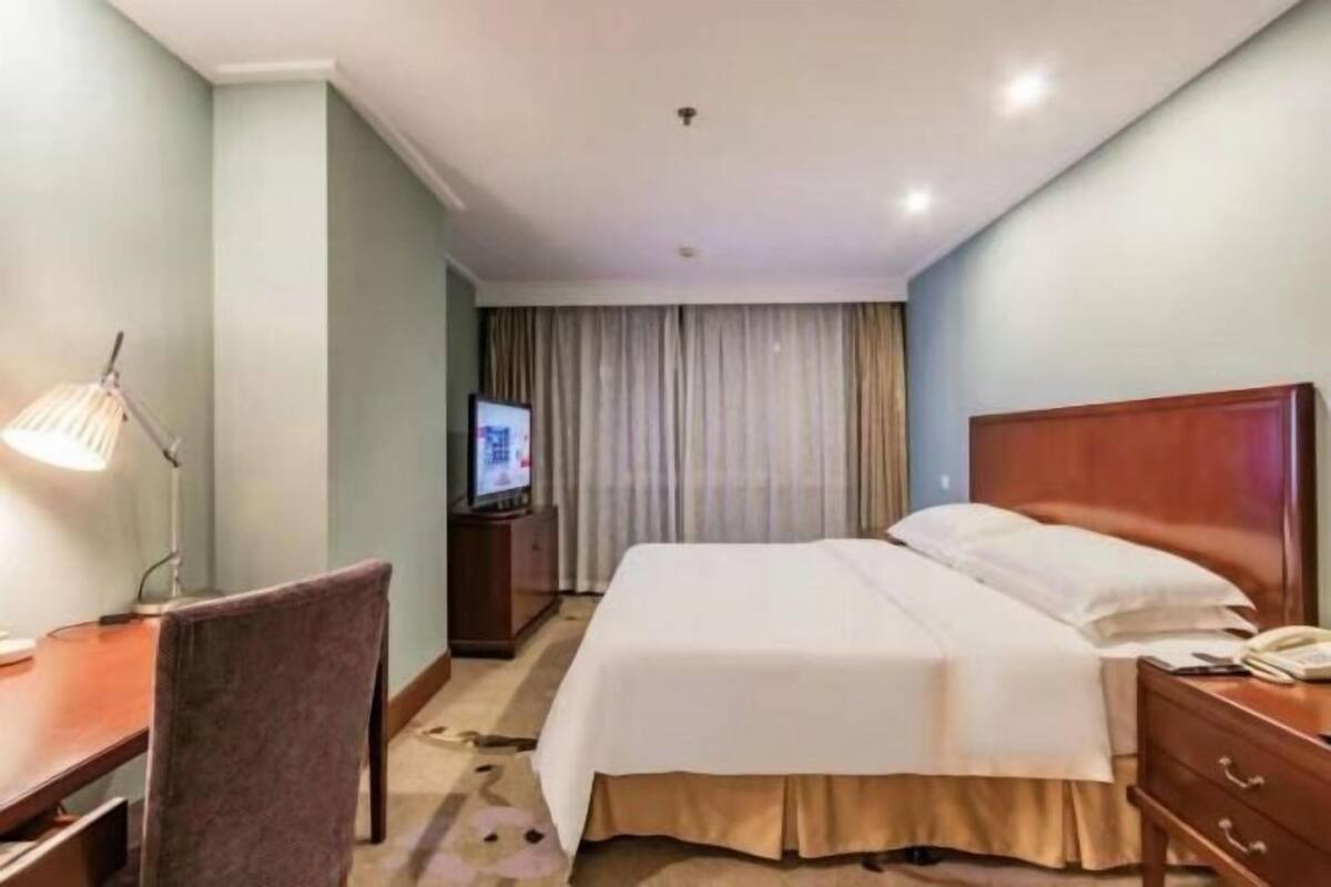 Ein Hotelzimmer mit Bett, Schreibtisch, Stuhl, Fernseher und Vorhang.