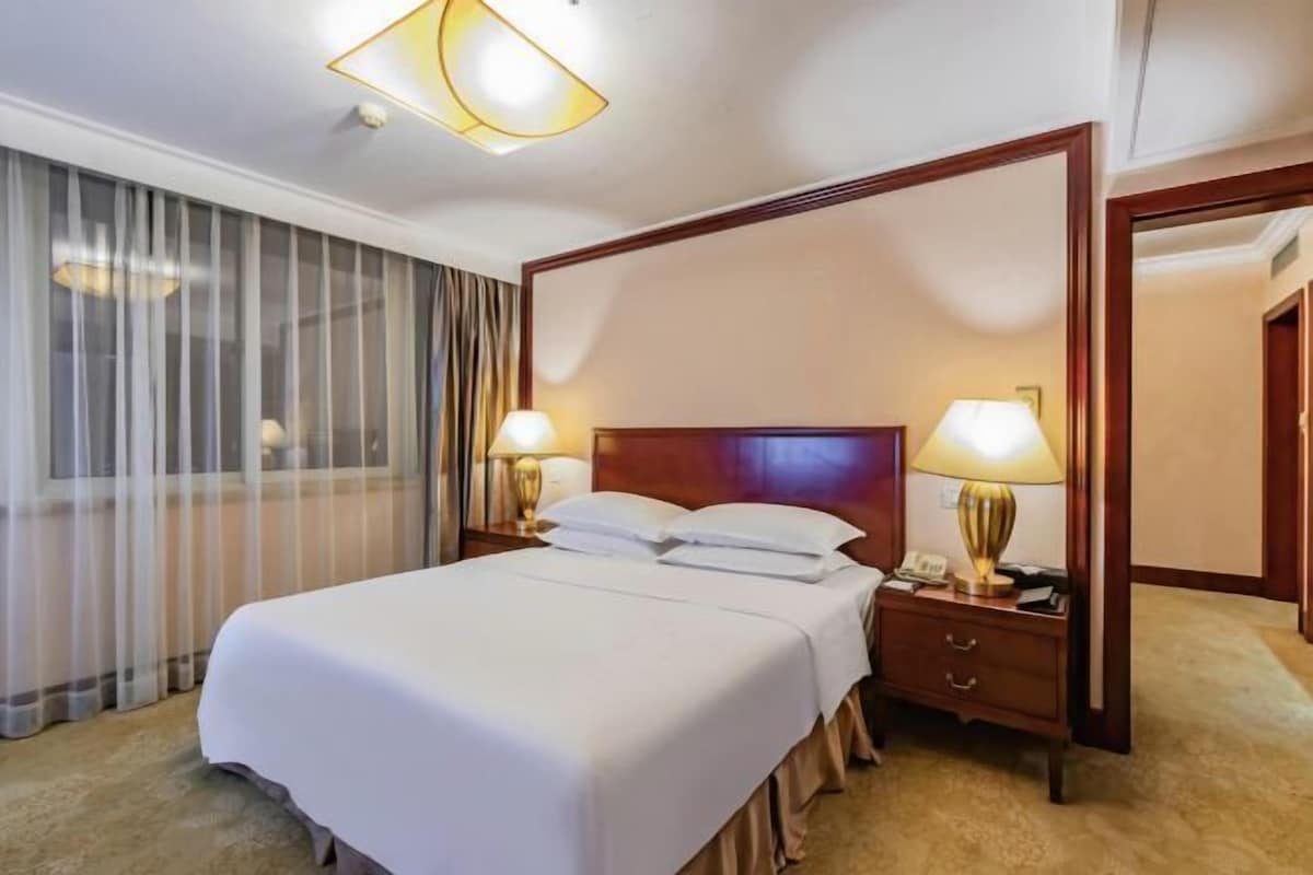 A hotel room with a large bed, two bedside lamps, a wooden headboard, a nightstand, and a large mirror.
