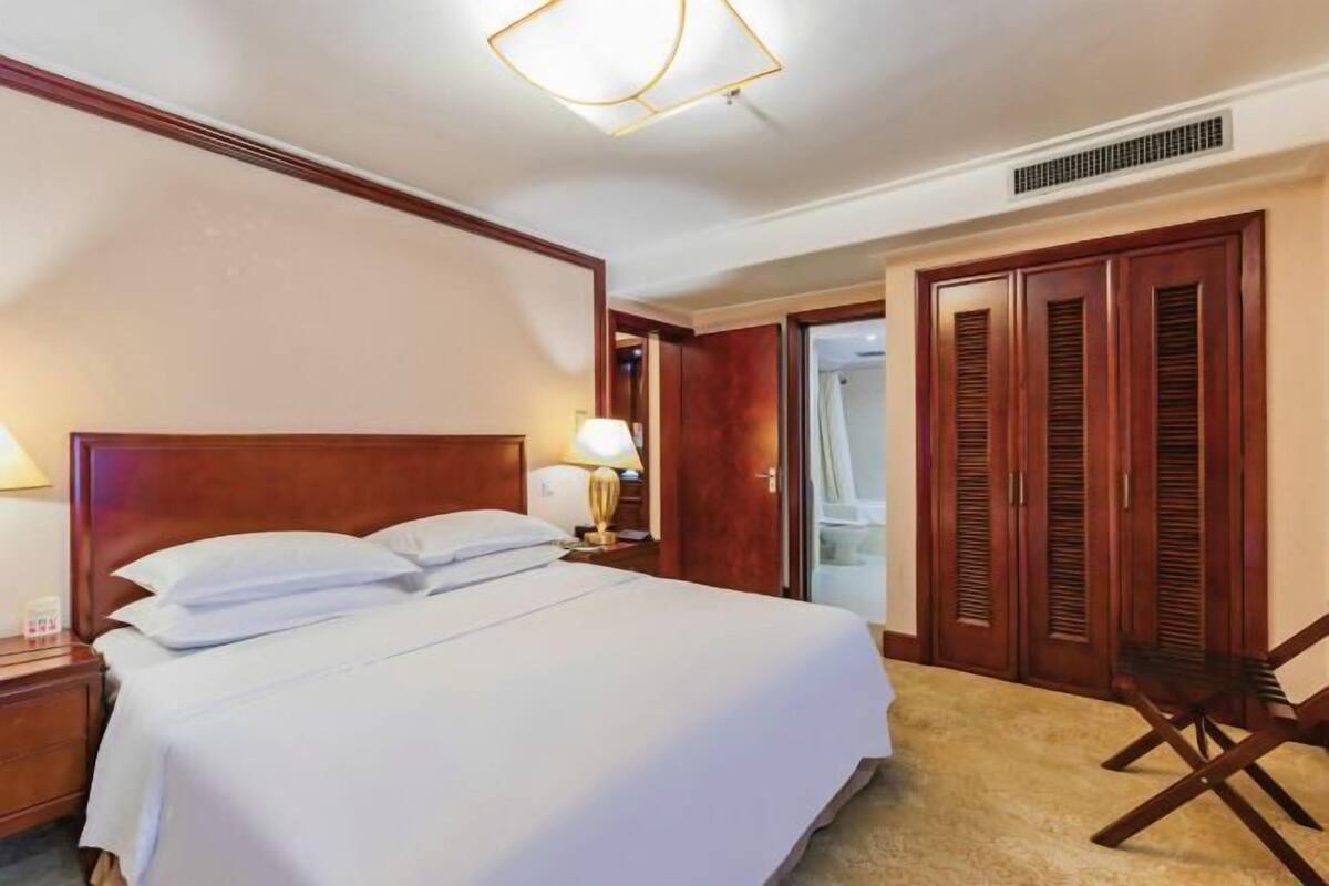 Ein Hotelzimmer mit einem großen Bett, einem Holz-Kopfteil, einem Nachttisch mit Lampe, einem Kleiderschrank und einem Sessel.