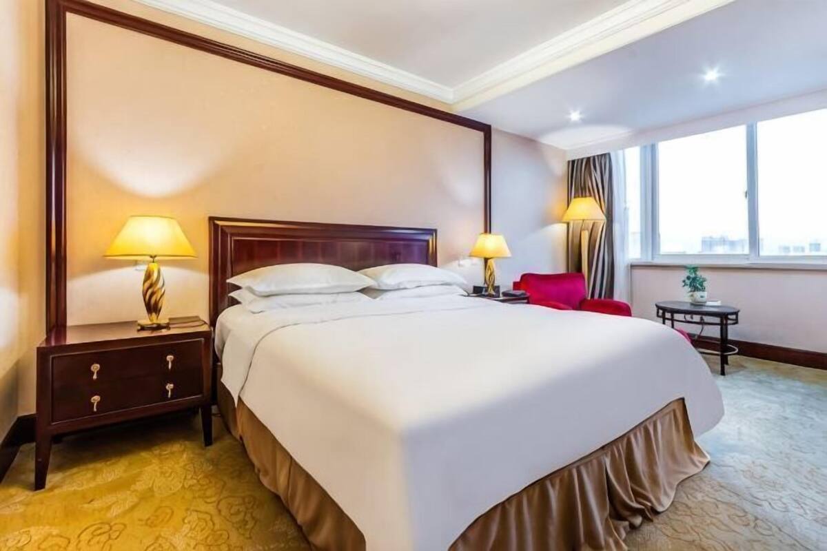 Ein Hotelzimmer mit einem großen Bett, zwei Nachttischen mit Lampen, einem kleinen Tisch mit einer Pflanze und einem Fenster mit Blick.