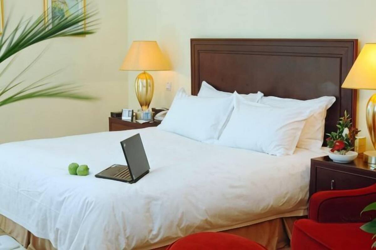 Ein Hotelzimmer mit einem Bett, zwei Nachttischlampen, einem Laptop auf dem Bett und einem roten Sessel.