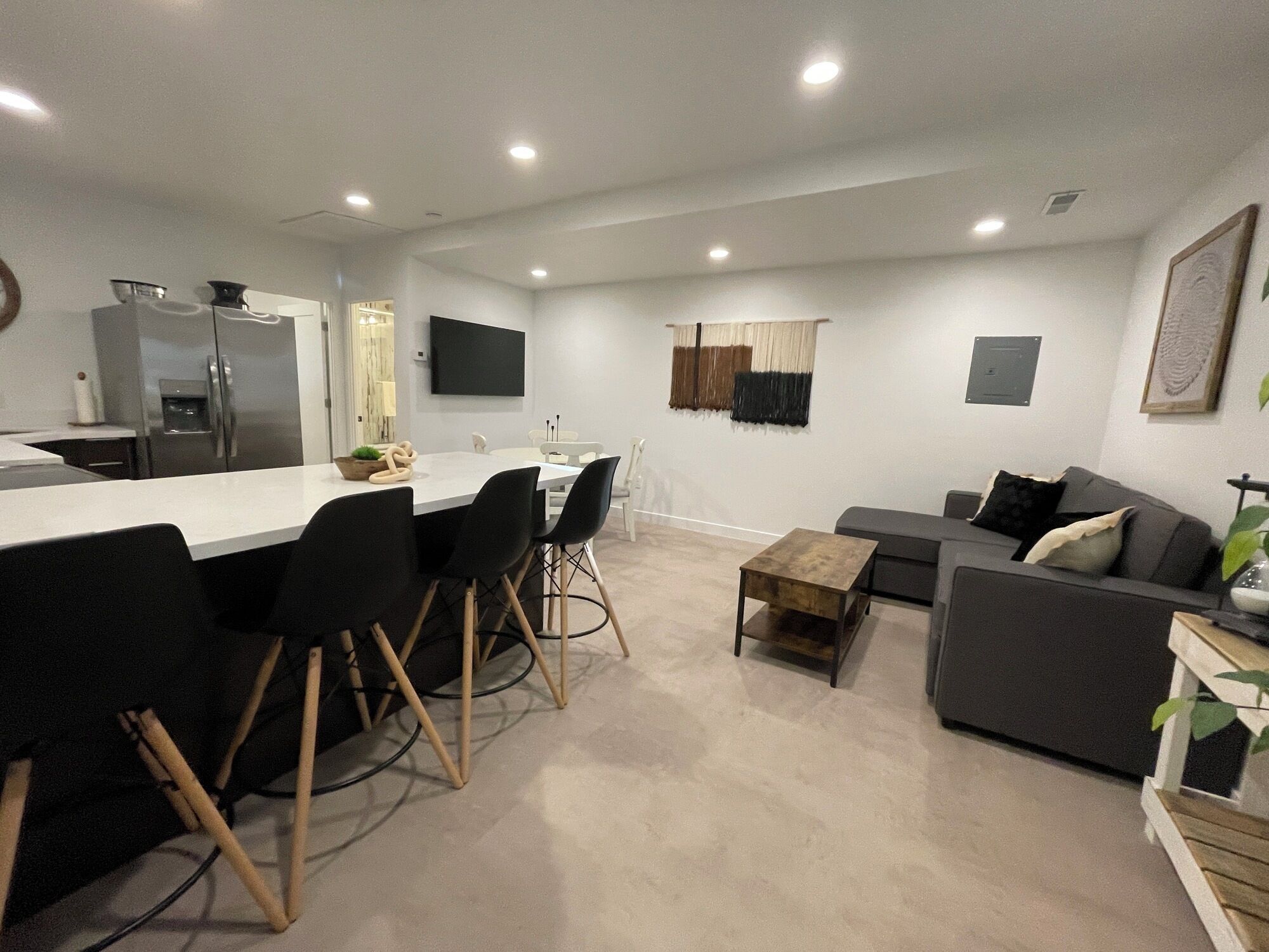 A modern living room with a dining area, a sofa set, and a kitchen with a refrigerator and a flat-screen TV.