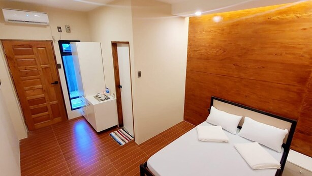 Un dormitorio con cabecera de madera, cama con ropa de cama blanca, una mesita de noche pequeña y un armario de madera.