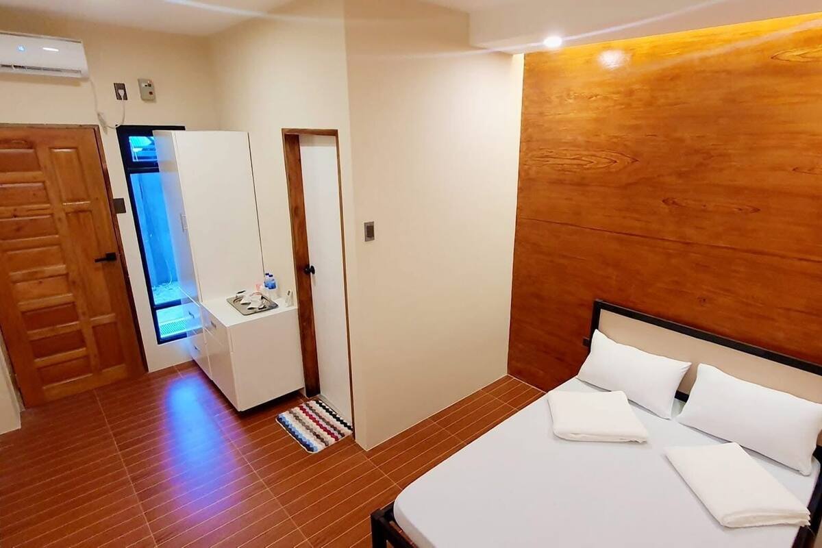 A bedroom with a wooden headboard, a bed with white linens, a small bedside table, and a wooden wardrobe.