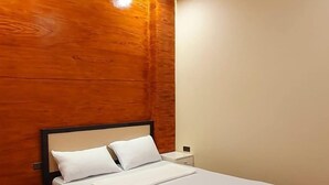 Una cama individual con cabecera de madera, ropa de cama blanca y una mesita de noche con lámpara.