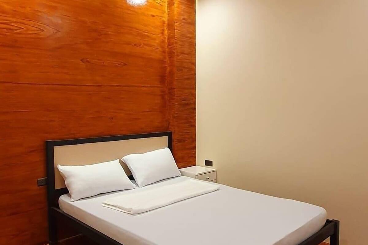 A single bed with a wooden headboard, white bedding, and a nightstand with a lamp.