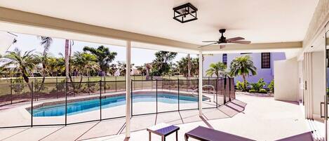 A covered outdoor area with a pool, lounge chairs, and a ceiling fan.