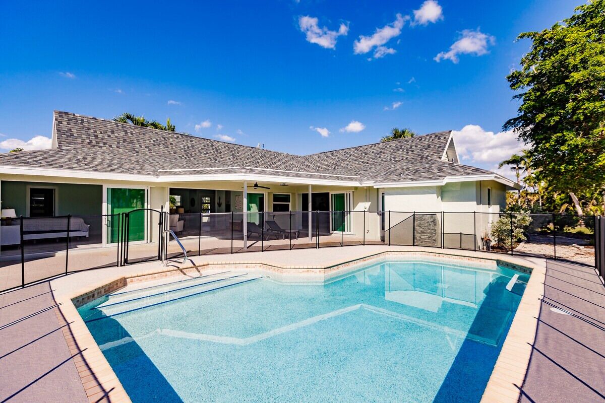 A poolside area with a rectangular pool, a covered seating area, and a building with a grey roof.