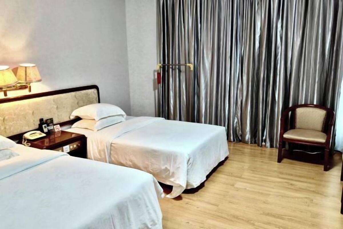 A hotel room with two beds, a nightstand with a lamp, a chair, and a curtain.